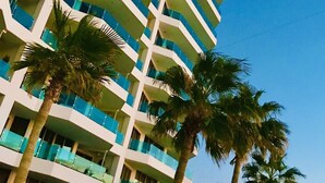 A multi-story hotel with balconies, palm trees, and a view of the ocean.