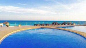 A pool with lounge chairs and a view of the sea.