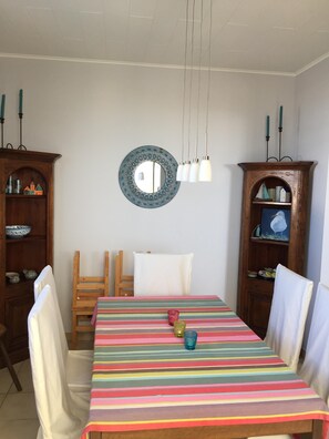 Uma sala de jantar com toalha de mesa listrada, cadeiras de madeira, um espelho e luminárias pendentes.
