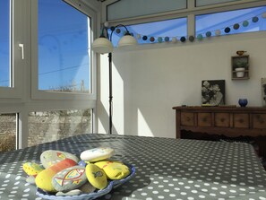 Quarto com toalha de mesa de bolinhas, janela com persianas, luminária fixada na parede, armário de madeira e quadro emoldurado.
