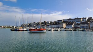 Un port de plaisance avec des bateaux amarrés, une ville riveraine avec des bâtiments et un ciel dégagé.
