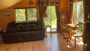 L’intérieur chaleureux d’un chalet avec un canapé en cuir, une table à manger et des chaises. Une pancarte sur le canapé indique : « Parc national ».