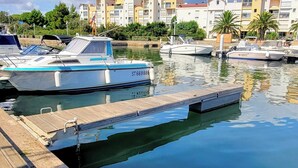 Ein Hafen mit mehreren angedockten Booten, einer hölzernen Anlegestelle und einer Reihe von Wohnhäusern im Hintergrund.