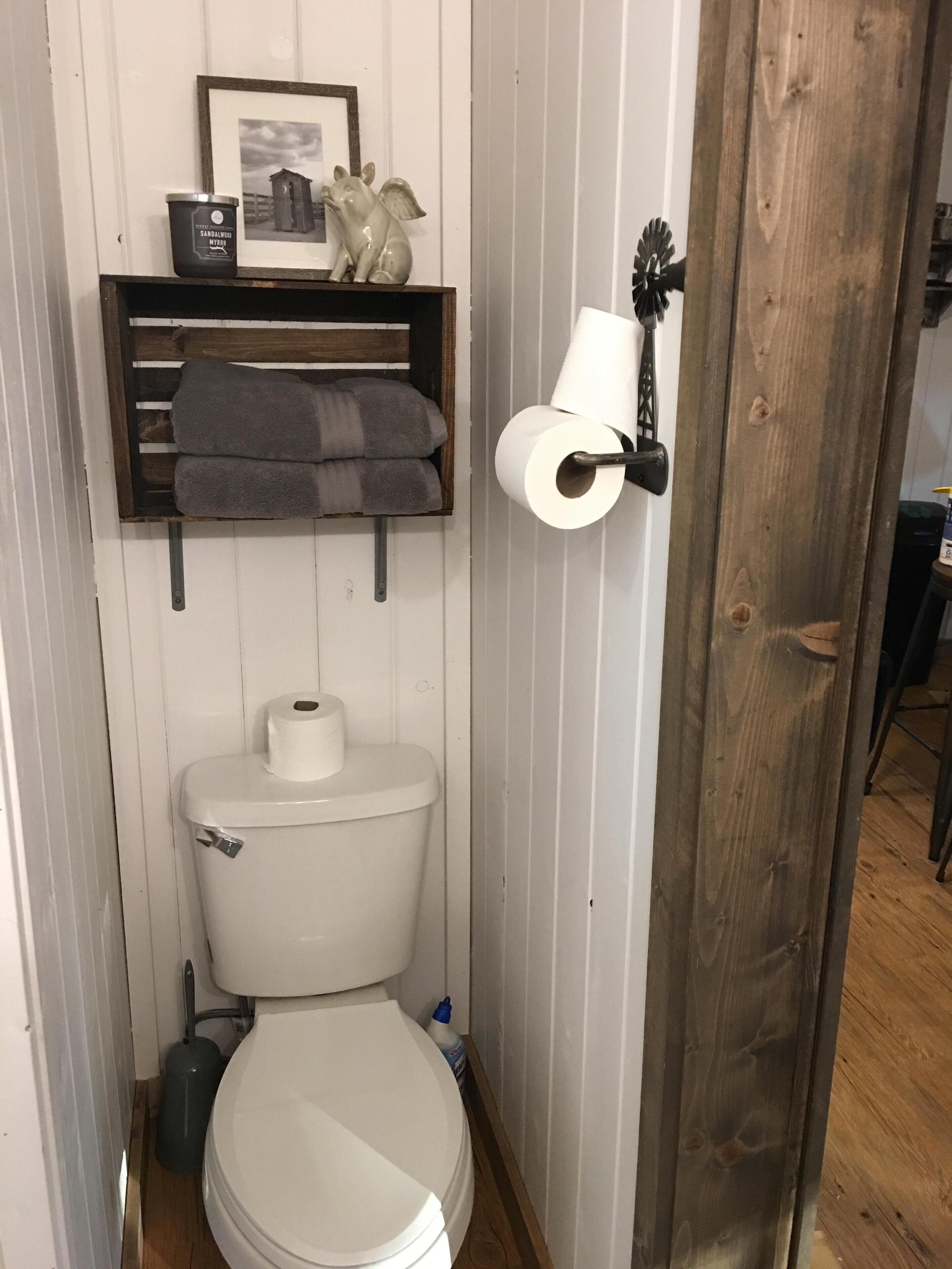 Een kleine badkamer met een wit toilet, een plankje met handdoeken, een lijst met een foto en een wc-papierhouder.