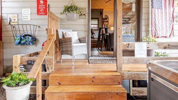 A wooden deck with a staircase leading to a covered area, a seating area with a table and chairs, and an American flag. - Guest Cottage,Dog friendly, minutes to Clayton, fenced yard, hot tub on patio. (Tiger)