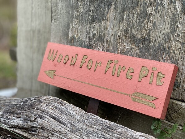 A wooden sign with the text "Wood For Fire Pit" and directional arrows.