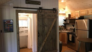 A rustic kitchen with wooden cabinets, a stainless steel refrigerator, and a wooden door leading to another room. - Guest Cottage,Dog friendly, minutes to Clayton, fenced yard, hot tub on patio. (Tiger)