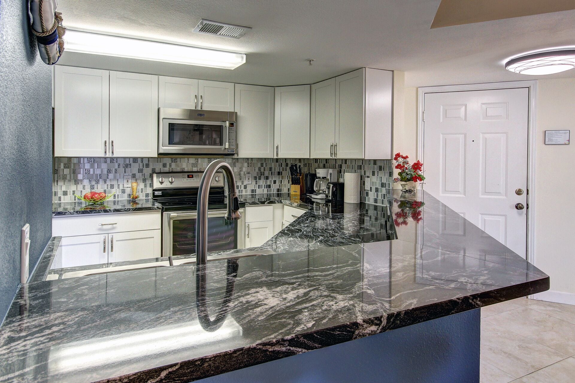 A modern kitchen with white cabinets, a stainless steel range, a microwave, and a black marble countertop.