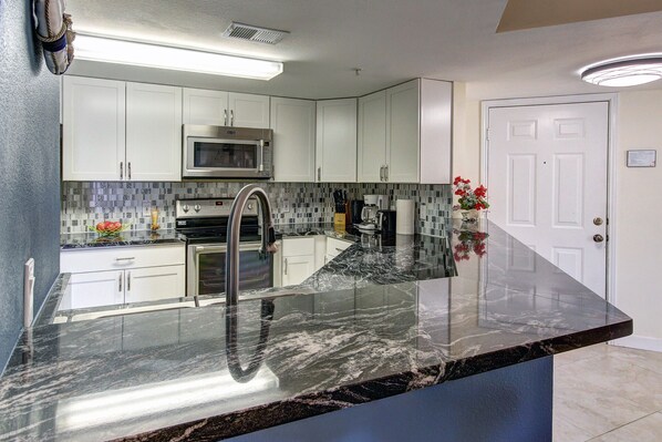 A modern kitchen with white cabinets, a stainless steel range, a microwave, and a black marble countertop.