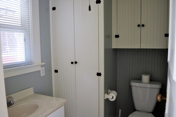 A bathroom with a toilet, sink, and window with blinds. - SEAHORSE COTTAGE - Adorable Cottage!! 15 seconds to beach access (Seaside)