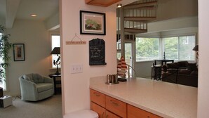 A kitchen with a white countertop, wooden cabinets, and a hanging sign. There is a dining area with a table and chairs, a staircase, and a window with blinds. - 3Bed/2Ba Absolutely Beautiful Home just off Prom with Ocean Views (Seaside)
