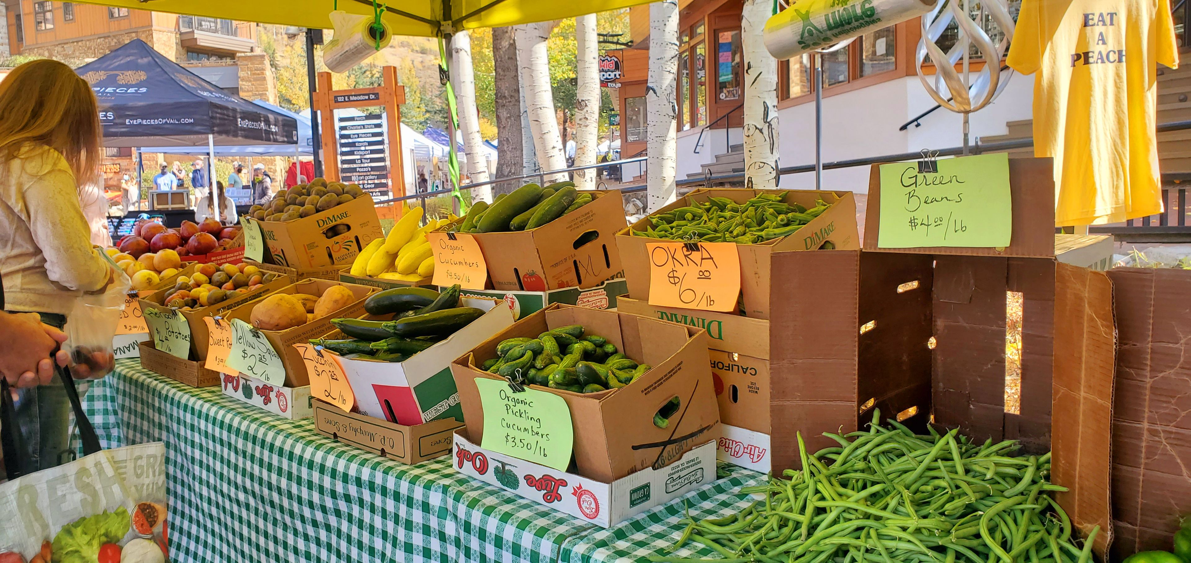 Un puesto de mercado con diversos vegetales y frutas, incluyendo pepinos, calabacines y plátanos, con etiquetas de precio.