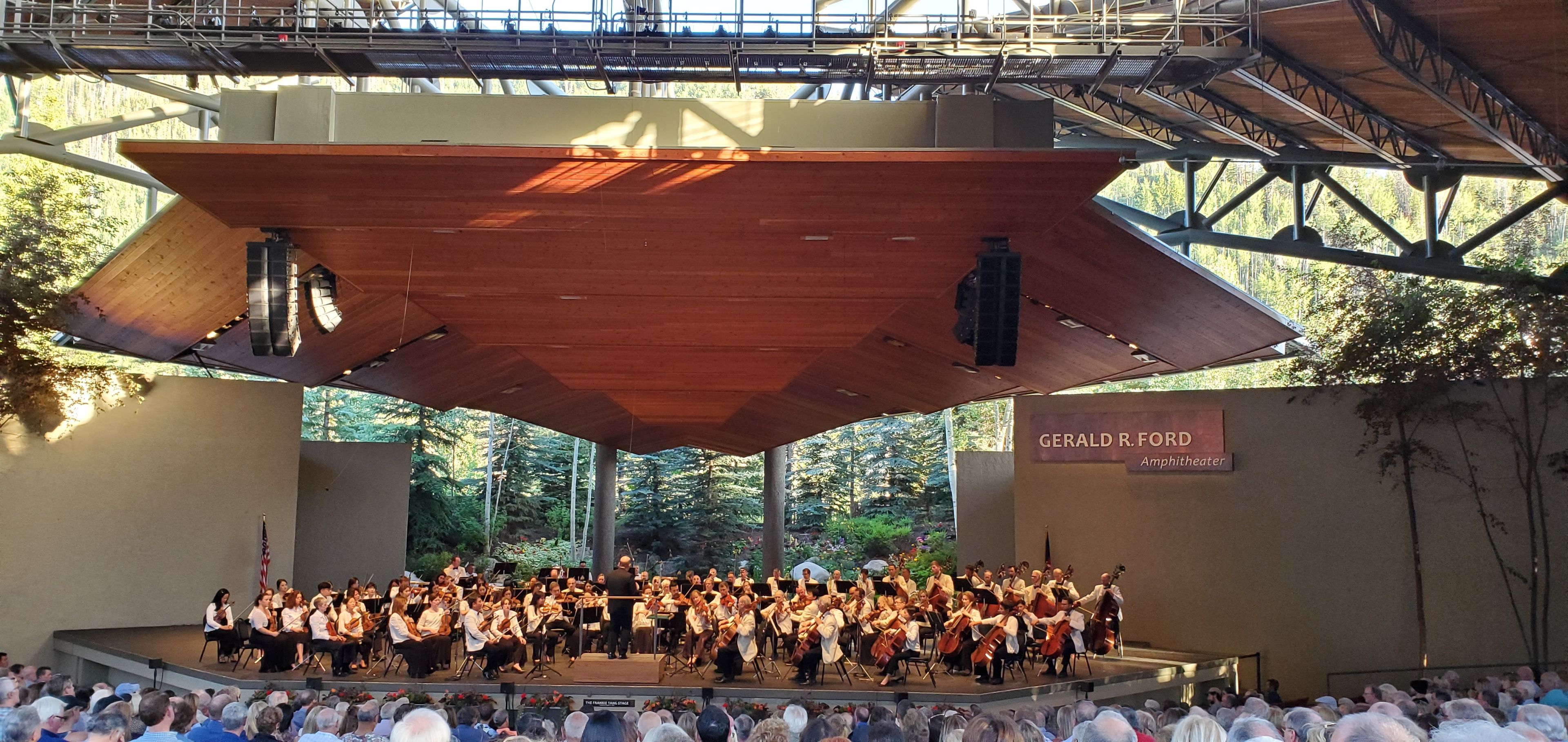 An outdoor amphitheater with a large audience and a stage for a musical performance.