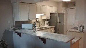 A kitchen with white cabinets, a stainless steel refrigerator, a coffee maker, and a sink. - Beachfront in the heart of Gulf Shores (Gulf Shores)