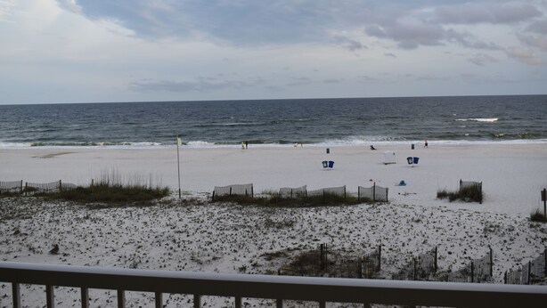 A beach with a sandy shore, a wooden fence, and a few beachgoers. - Beachfront in the heart of Gulf Shores (Gulf Shores)