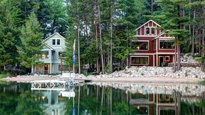 A lakeside cabin with a dock, surrounded by dense forest. - Newly Built Luxury Lakefront Cottage with Fire Pit, Dock, Game Room (Traverse City)