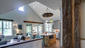 A spacious kitchen with a large island, wooden cabinets, and a dining area with blue chairs. - Newly Built Luxury Lakefront Cottage with Fire Pit, Dock, Game Room (Traverse City)