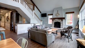 A spacious living area with a fireplace, a staircase, and a dining area. - Newly Built Luxury Lakefront Cottage with Fire Pit, Dock, Game Room (Traverse City)