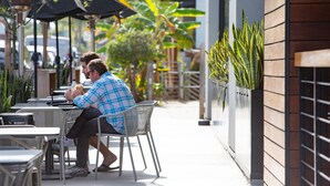 A man sitting at an outdoor cafe with tables and chairs, surrounded by plants and umbrellas. - Spacious Ocean Oasis with Private Outdoor Shower! (Encinitas)