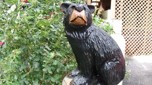 Una estàtua d'ós negre sobre un pedestal blanc, envoltada de vegetació.