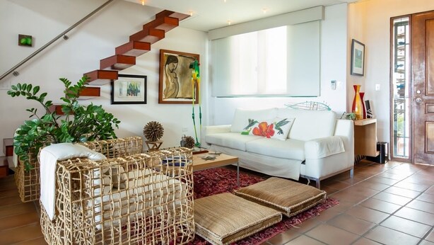 Una sala de estar moderna con un sofá blanco, una escalera de madera y un ventanal grande.