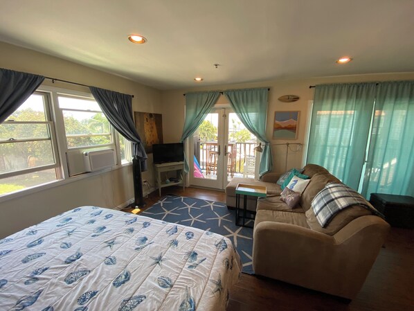 A room with a bed, a sofa, a TV, and a balcony with curtains.