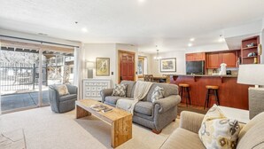 A spacious living room with a grey sofa, a wooden coffee table, and a view of the outdoor balcony. - All Seasons 2BR | Walk to Park City Mountain | Heated Pool | Sleeps 6 (Park City)