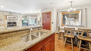 A kitchen with granite countertops, a double sink, wooden cabinets, a stone accent wall, and a dining area with a wooden table and chairs. - All Seasons 2BR | Walk to Park City Mountain | Heated Pool | Sleeps 6 (Park City)