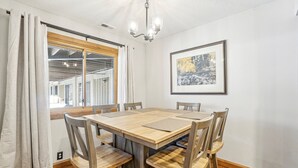 A dining area with a wooden table and chairs, a chandelier, a framed painting, and a window with curtains. - All Seasons 2BR | Walk to Park City Mountain | Heated Pool | Sleeps 6 (Park City)