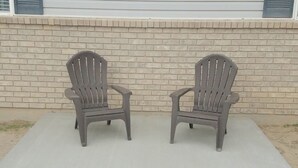 Dos sillas Adirondack en un patio de concreto con un muro de ladrillo al fondo.