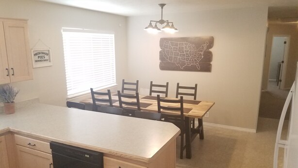 Una cocina con isla central, armarios de madera, lavavajillas y una mesa de comedor con sillas.