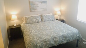 Un dormitorio con una cama, dos mesitas de noche con lámparas, un cuadro en la pared y una ventana.