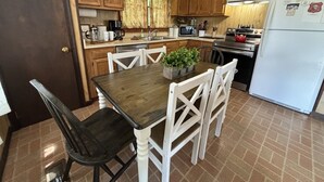 Una cocina con armarios de madera, una mesa de comedor con sillas, un refrigerador y una cafetera.