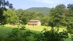 Una casa de dos pisos con balcón, rodeada de un paisaje verde exuberante y una colina al fondo.
