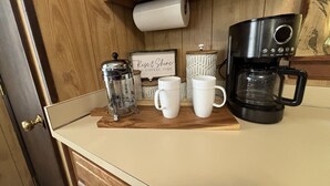 Una encimera de cocina con una cafetera, dos tazas blancas, una prensa francesa y un letrero que dice "Rise & Shine".