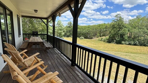 Un porche de madera con mecedoras, una mesa y vistas a un campo cubierto de césped y árboles.