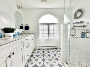 Un baño con tocador blanco, un espejo grande, una ventana con vistas y zona de ducha con puerta de cristal.