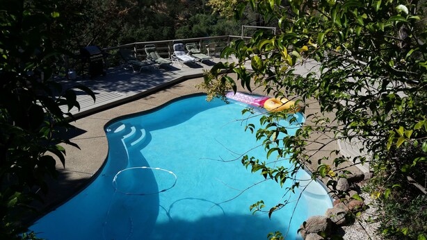 A swimming pool with lounge chairs and inflatable rings, surrounded by trees and a deck. - A Great Home in a Resort-Like Setting--
Private Retreat with pool & River Views (Valley Springs)