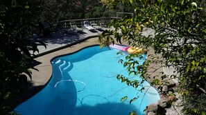 A swimming pool with lounge chairs and inflatable rings, surrounded by trees and a deck.