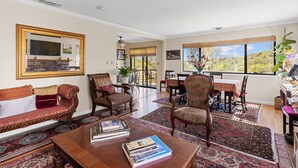 A spacious living room with a sofa, armchairs, a coffee table with books, a fireplace, and large windows offering a view of the outdoors. - A Great Home in a Resort-Like Setting--
Private Retreat with pool & River Views (Valley Springs)