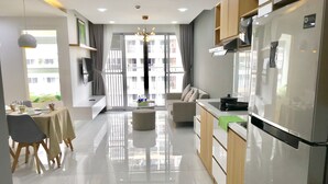 Eine moderne Küche mit einem großen Kühlschrank, ein Essbereich mit Tisch und Stühlen sowie eine Wohnarea mit Sofa und Couchtisch.