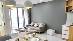 Ein modernes Wohnzimmer mit grauem Sofa, einem Esstisch gedeckt mit Tellern, Tassen und Besteck sowie einer Küchenzeile mit Holzschrank.