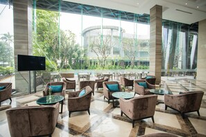 A spacious lobby with modern furniture, large windows, and a view of greenery and a building in the background. - The Mira Central Park Hotel (Bien Hoa)
