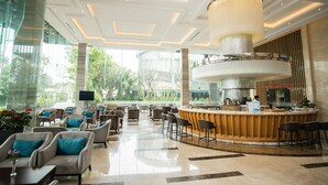 A spacious lobby with a central bar, comfortable seating, and large windows offering a view of greenery. - The Mira Central Park Hotel (Bien Hoa)