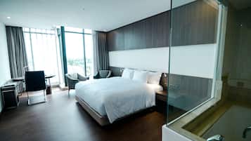 Et moderne hotelværelse med en stor seng, et badeværelse med glasvægge og et siddeområde med stol og bord.