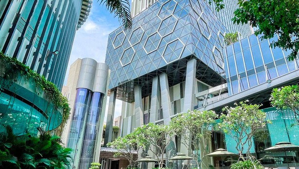 A modern building with a geometric facade, a pool area with lounge chairs and umbrellas, and lush greenery. - The Mira Central Park Hotel (Bien Hoa)