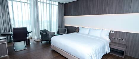 A modern hotel room with a large bed, a desk, and two chairs.