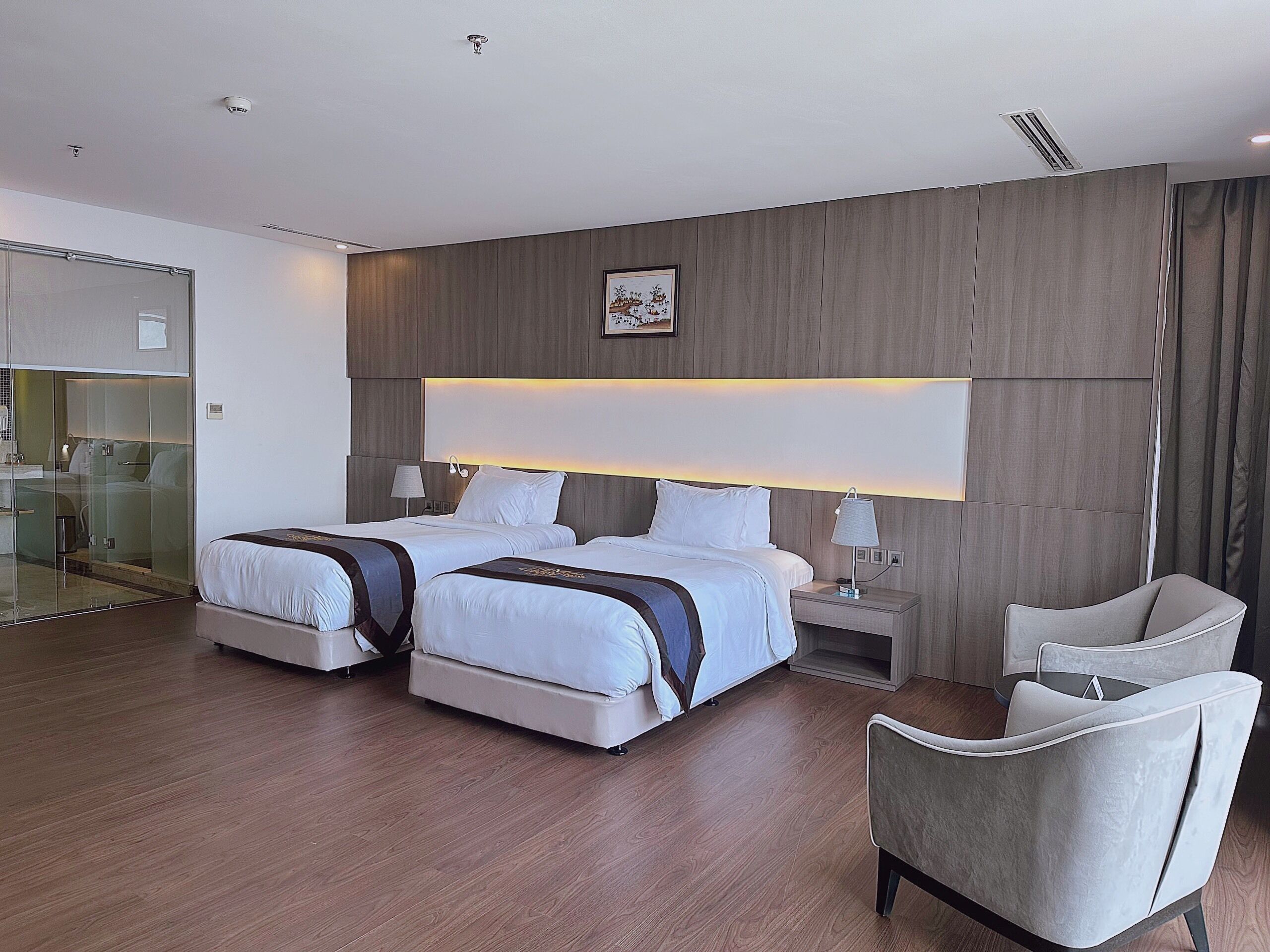 Una habitación de hotel moderna con dos camas, ducha con cerramiento de vidrio, escritorio y una silla.