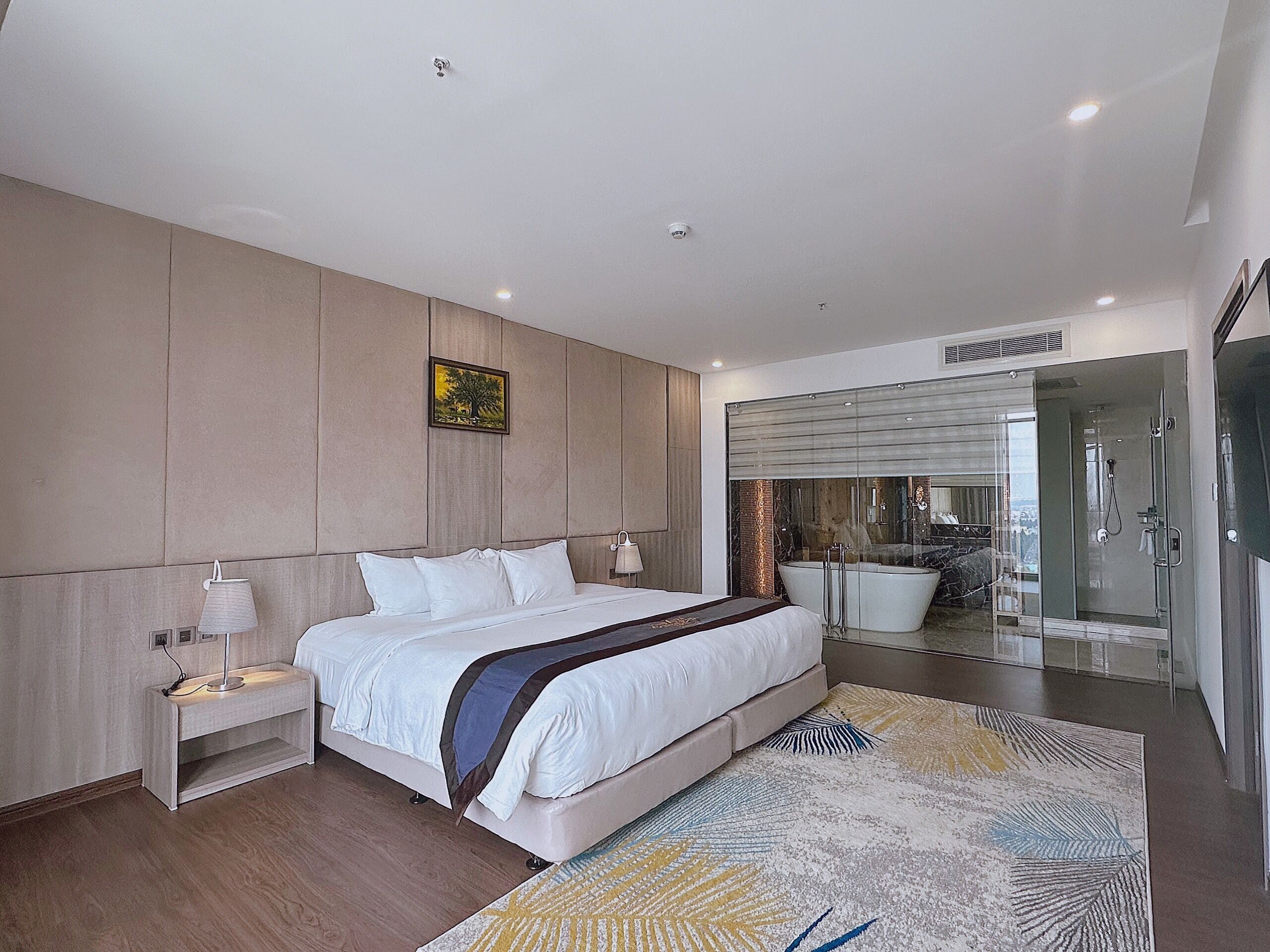 Un dormitorio moderno con una cama grande, mesitas de noche, cabina de ducha con vidrio y vista a la ciudad.