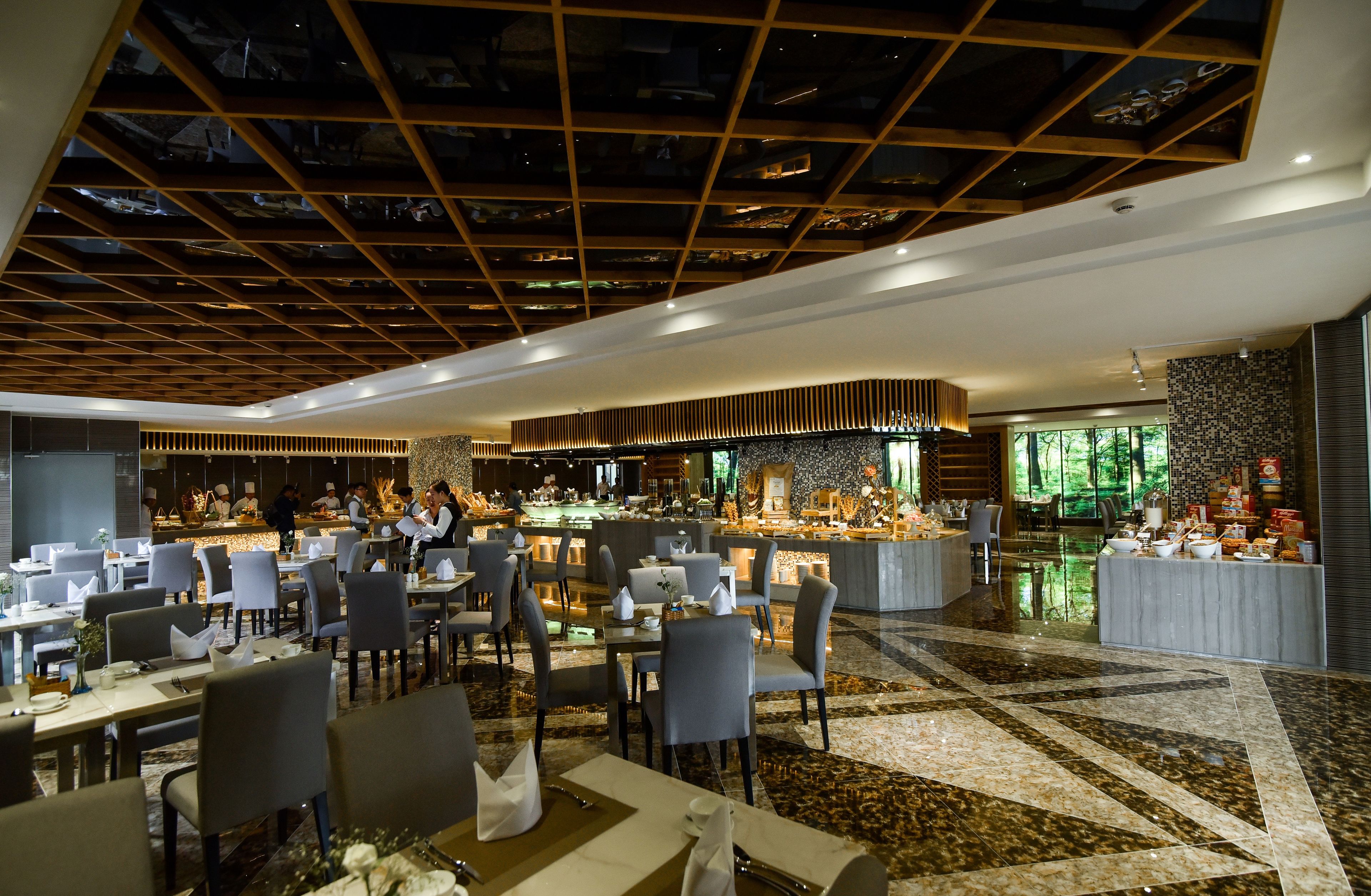 A modern restaurant with a central bar area, multiple dining tables, and a patterned floor.